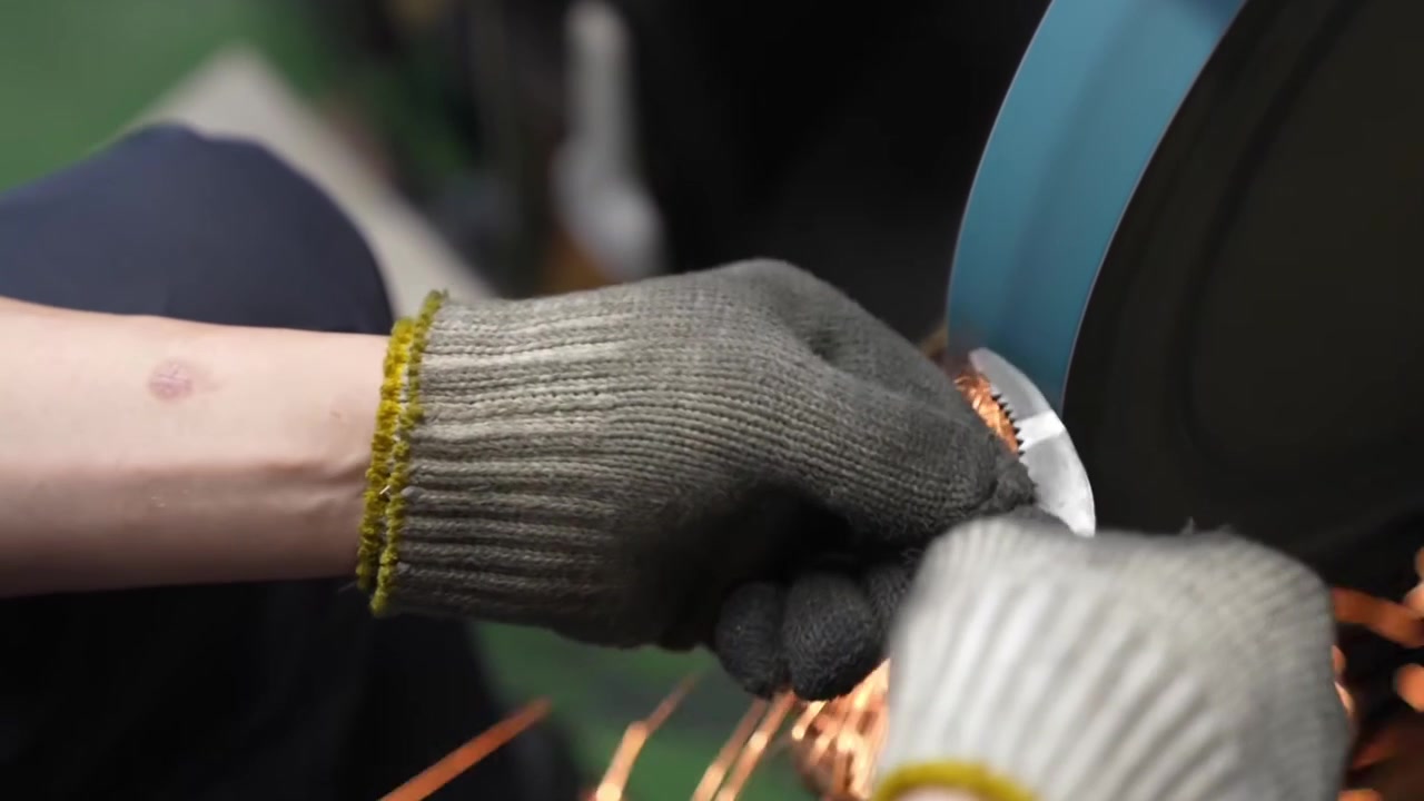 Nærbillede af arbejderhænder, der sliber tænger på en båndsliber med gnister, der flyver på fabrikken