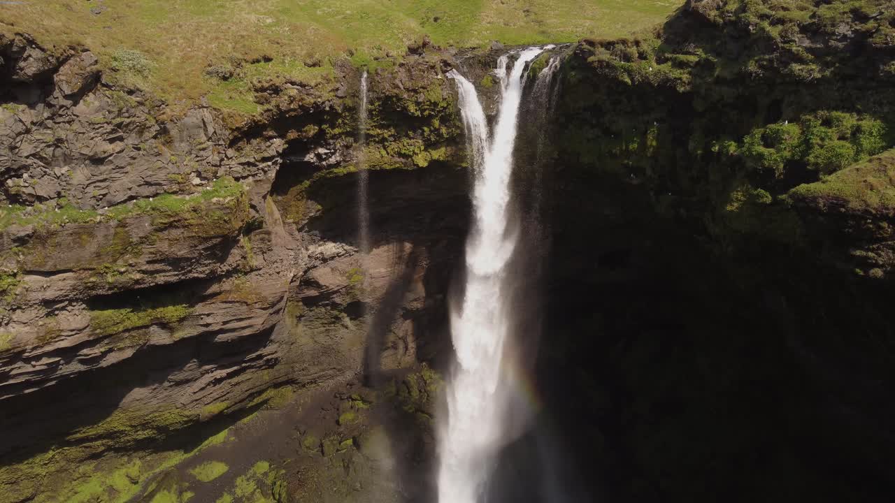 toma aérea de un dron de una hermosa cascada en islandia en un día soleado con pájaros volando y un pequeño arco iris