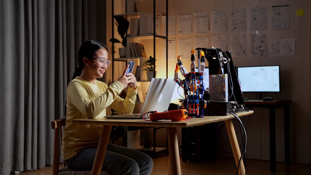 집에 있는 노트북에서 사이보그 손으로 작업하는 동안 스마트폰을 사용하는 아시아 십대 소녀