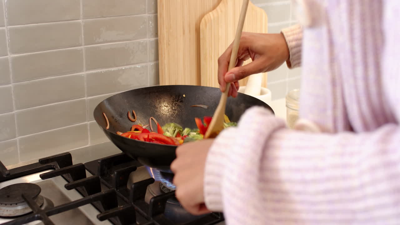 Cooking vegetables in wok on stove, hands stirring with wooden spoon