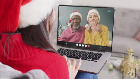 mujer caucásica con sombrero de santa teniendo llamada de video portátil con pareja feliz diversa