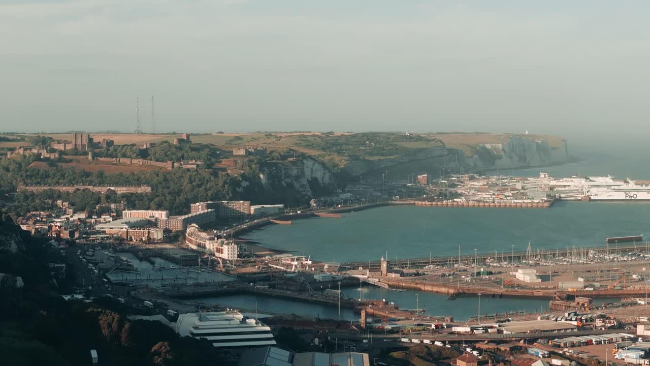 Drone ascends in wide circle around Dover area showing sea, town, and cliffs, establishing overview
