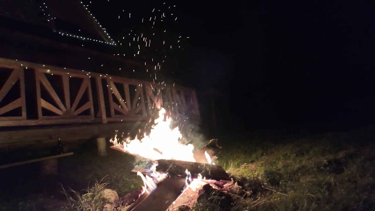 Grande falò che brucia in un prato erboso sotto il cielo notturno scuro. Bagliore caldo, braci volanti e atmosfera naturale all'aperto, ideale per immagini di viaggio, campeggio e avventura