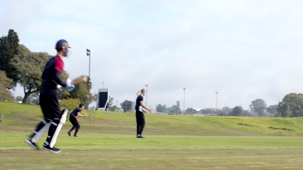 Two teams of multiracial male cricket players and male umpire playing cricket on pitch