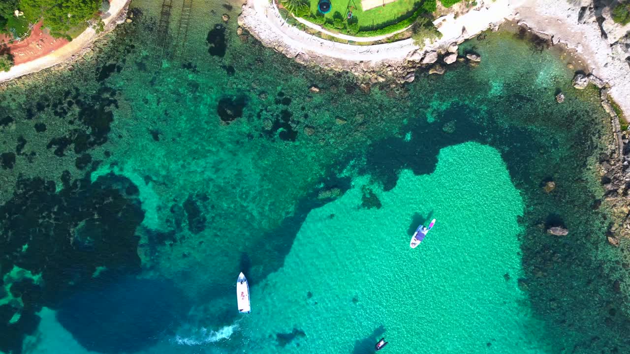 Barche a vela e yacht che galleggiano su acqua trasparente color turchese in una baia a Ibiza. Splendida vista aerea ripresa da drone con telecamera puntata verso il basso.