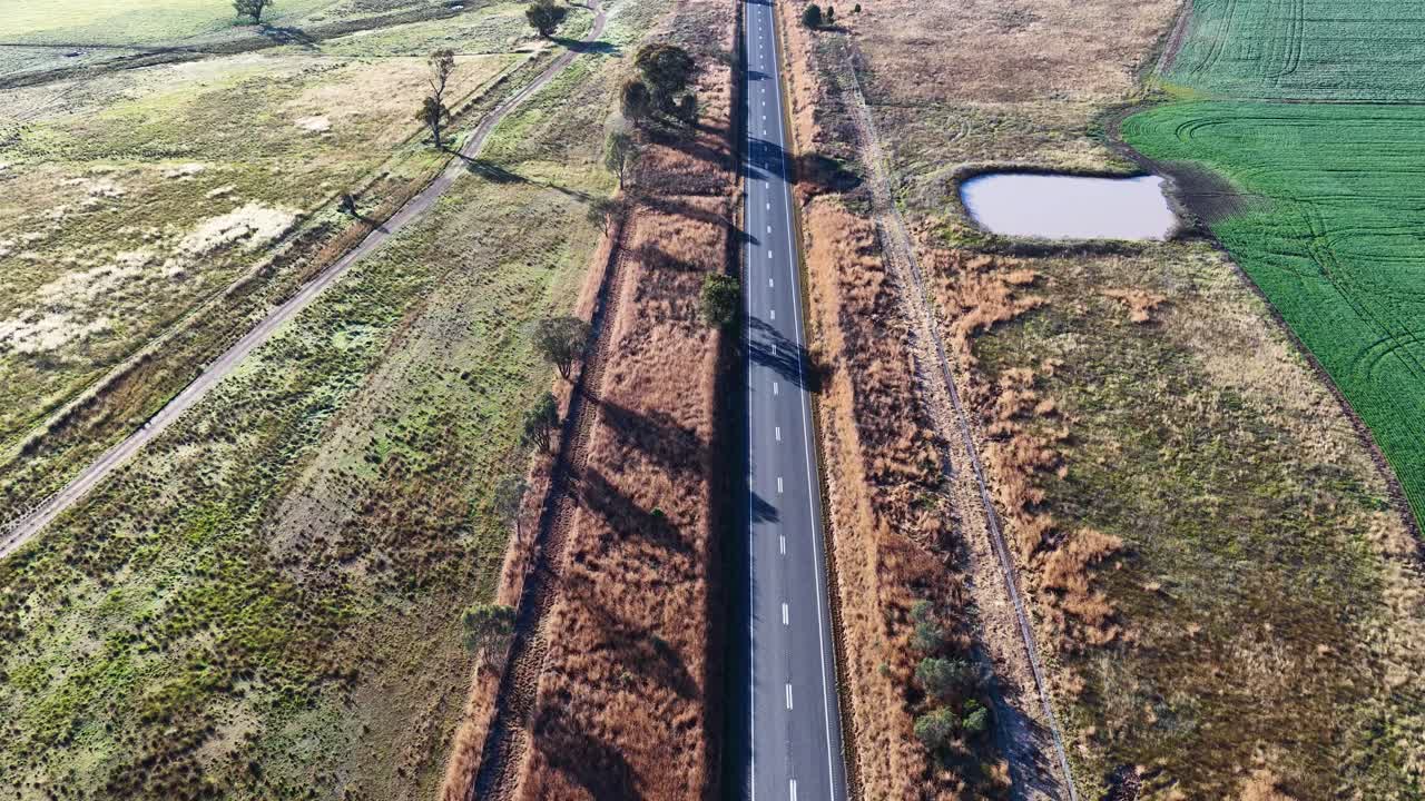 Drone footage of countryside road, fields, and water pond