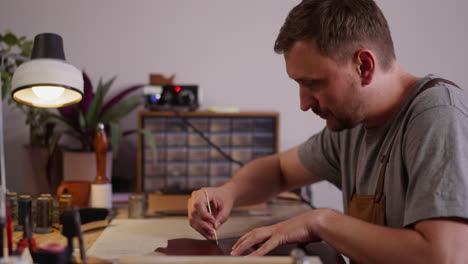 concentrated man cuts leather with small knife at workplace