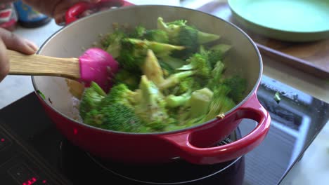 stirring broccoli in a red pot on an induction cooktop