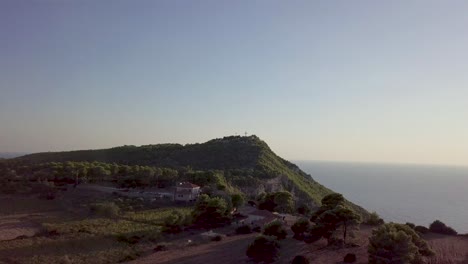 Drone-footage-of-hotel-at-the-foot-of-a-hill-near-the-coast-of-the-island-of-Zakynthos-Greece,-with-open-sea-in-the-background