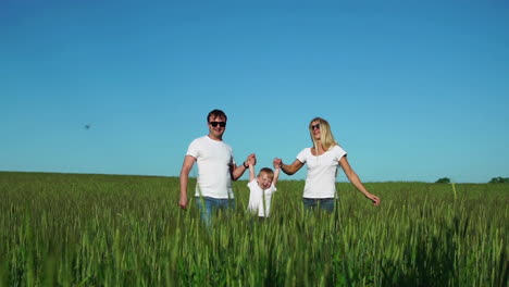 mother father and son walk in the field with spikes in white t-shirts and jeans fun swinging it on his hands