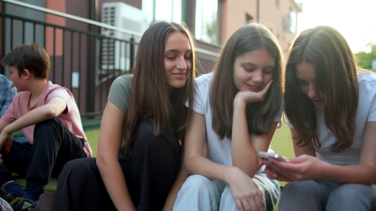 ученики-подростки развлекаются и разговаривают с помощью мобильных телефонов на школьном дворе