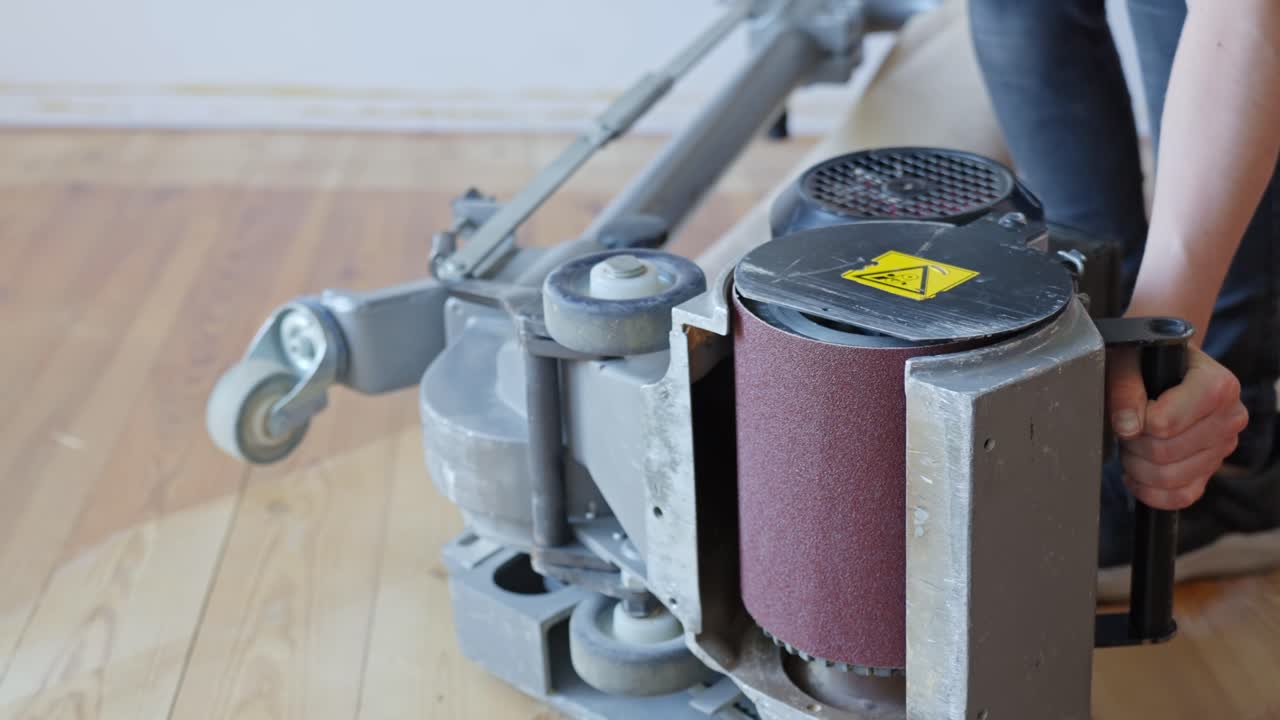 Technician flips heavy floor sanding machine on its side for maintenance and inspection