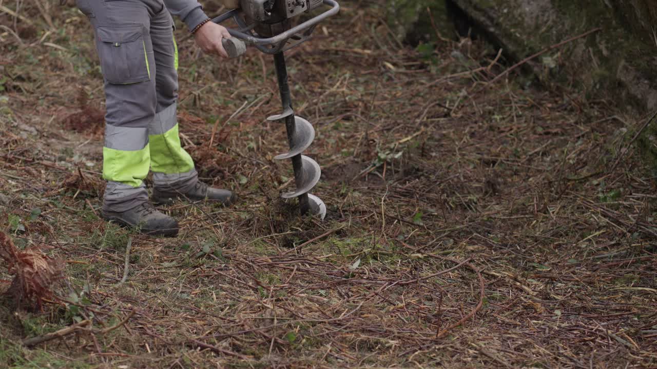«Persona perforando un agujero en el suelo con una barrena en un terreno forestal»
