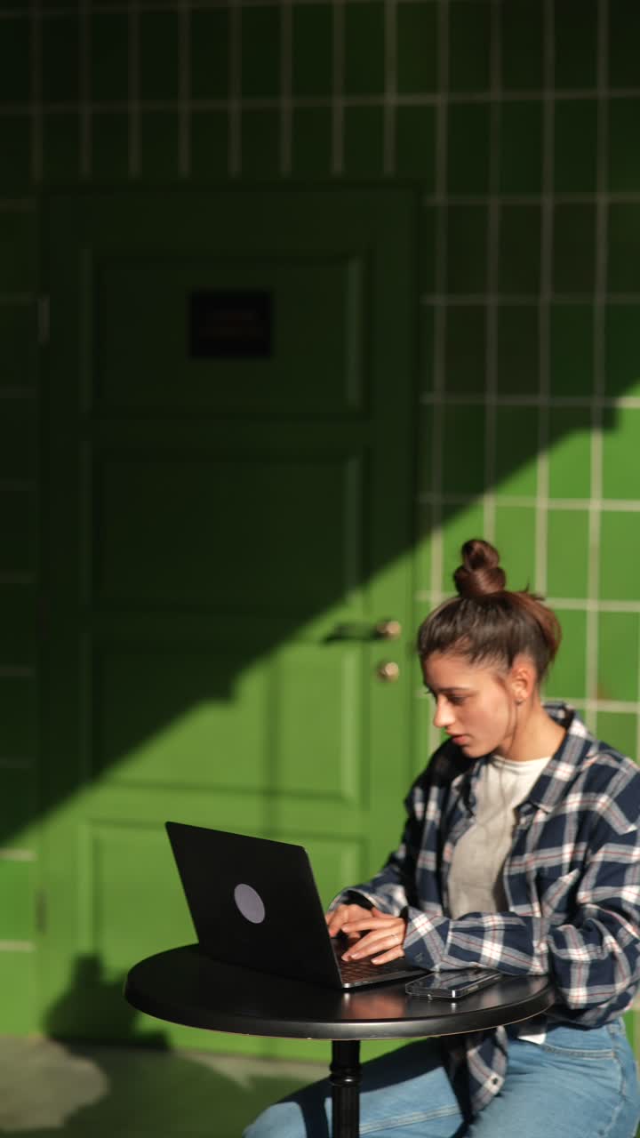 mujer joven trabajando en una computadora portátil en un café al aire libre