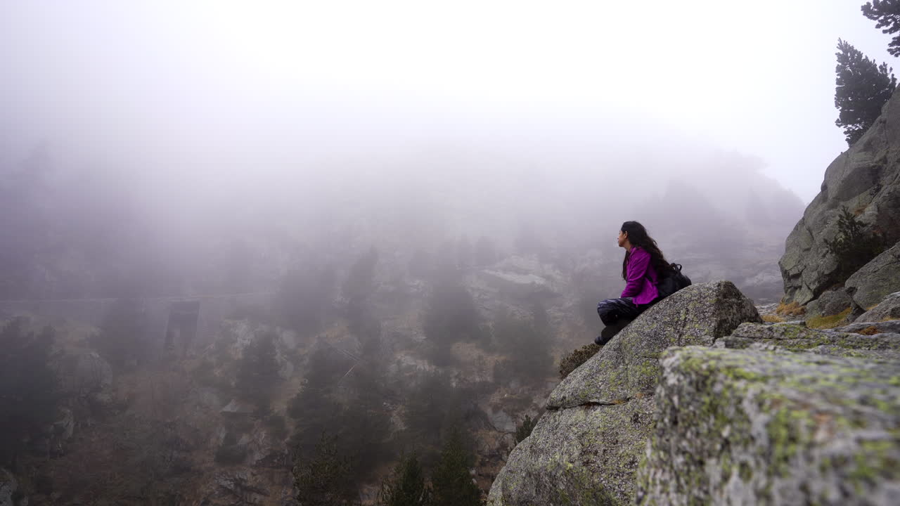 viajero solitario joven mochilero sentado solo en el borde del acantilado de montaña rocosa con paisaje natural brumoso