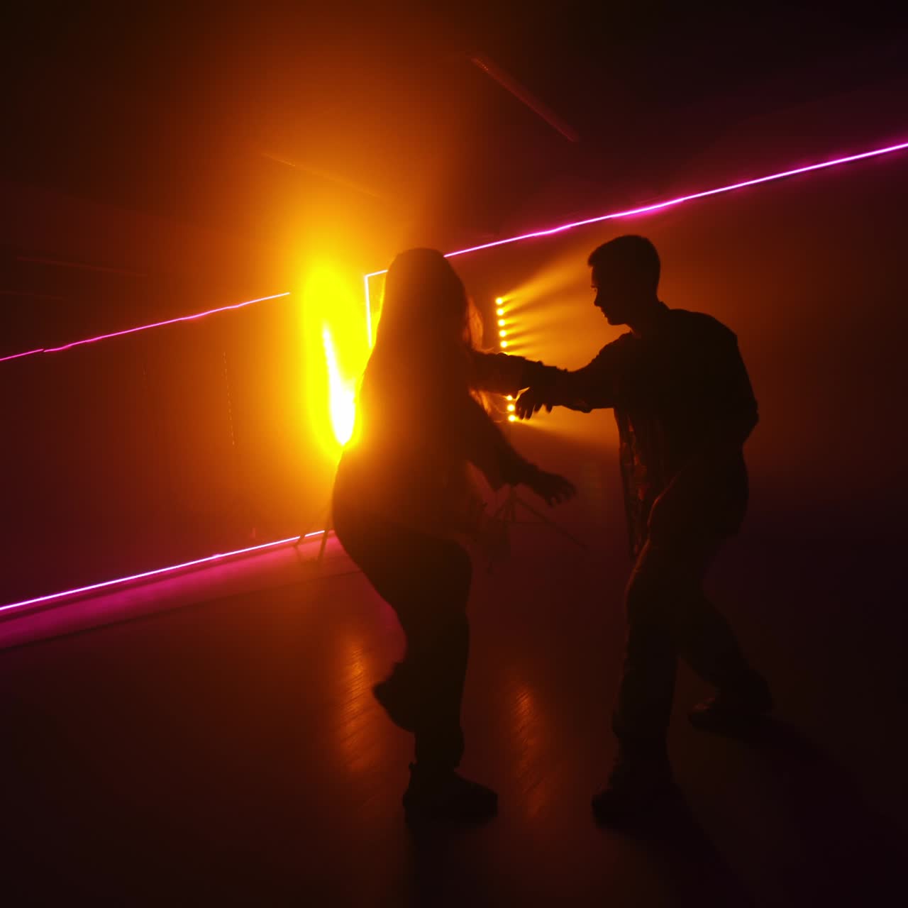 Couple silhouettes dancing in dark studio. Contemporary style performance. Yellow lamp and pink neon light at backdrop