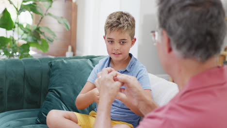 feliz abuelo caucásico y nieto sentados en el sofá y usando lenguaje de señas, cámara lenta