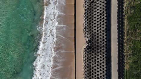top down of cronulla boardwalk and breakwater with crashing waves running parallel to beach and sea with visible wave lines, sydney nsw australia