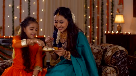 happy south indian family - beautiful girl choosing her favorite sweet from a plate - festive background