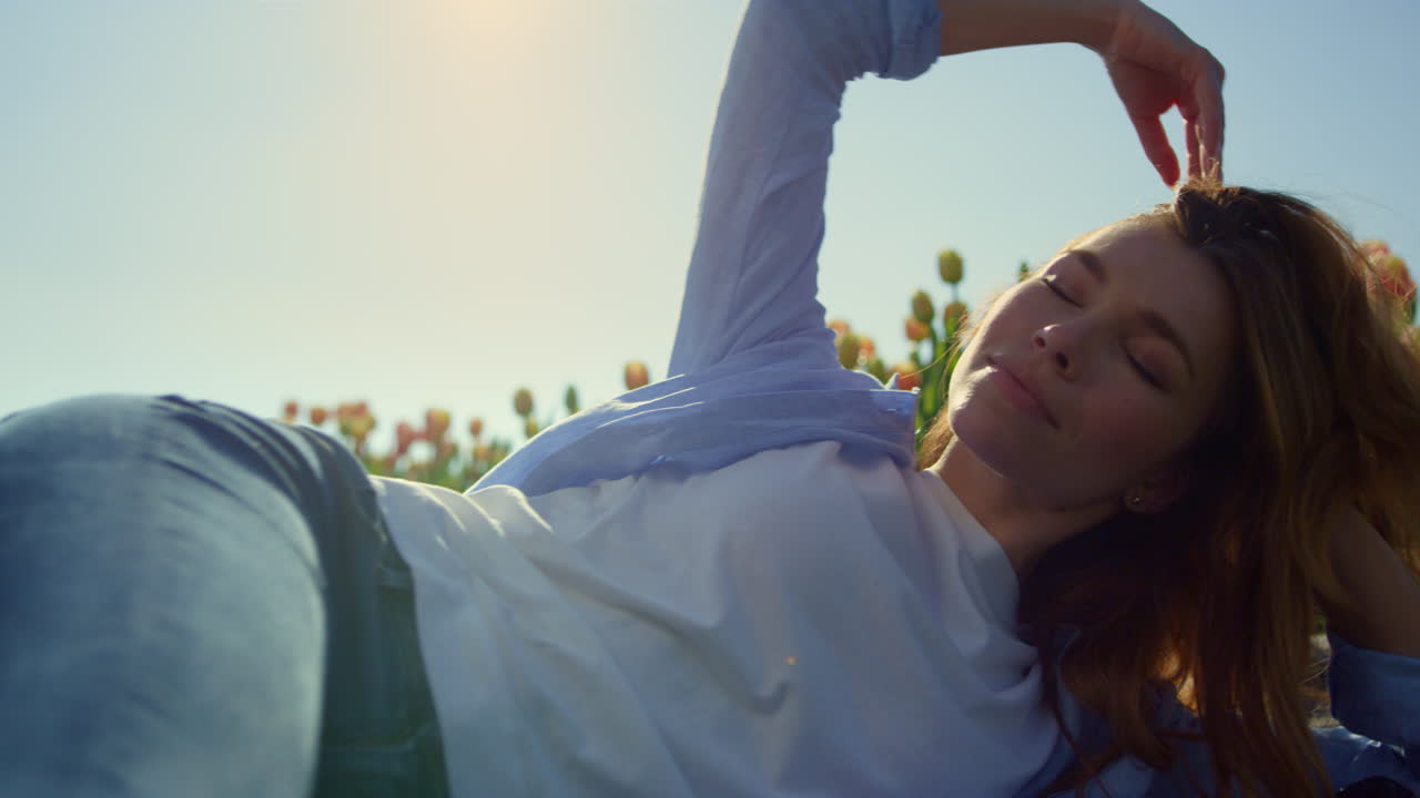 mujer relajada acostada en el jardín de tulipanes. mujer sonriente jugando con el cabello en la suave luz del sol.
