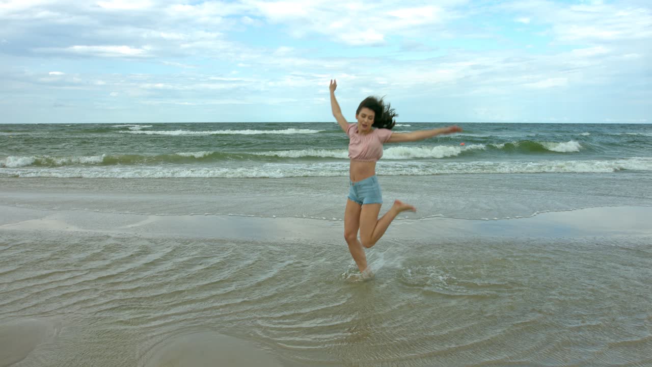 바다 해안에서 느린 동작으로 점프하고 춤을 추는 브루네트 댄서