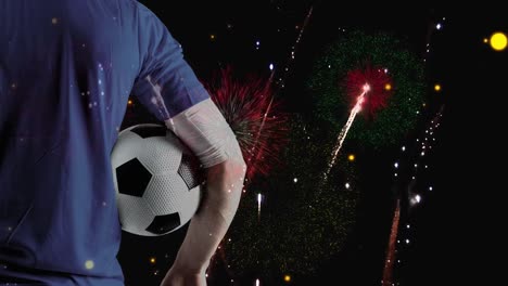 Animation-of-fireworks-over-back-view-of-caucasian-male-soccer-player-holding-ball