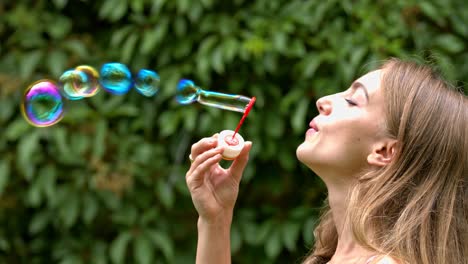 attractive woman on a summer day in the park is playing by blowing soap bubbles