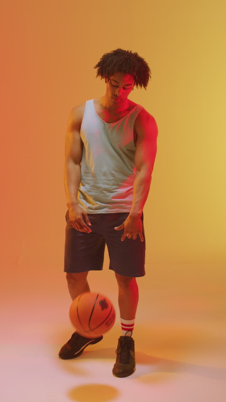 video vertical de un jugador de baloncesto masculino biracial con una pelota en un fondo naranja