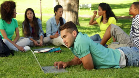 smiling student using his laptop in front of his friends