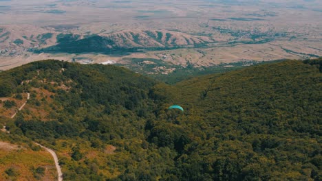 Calm-and-peaceful-flight-with-a-paraglider-over-a-forest-drone-shot