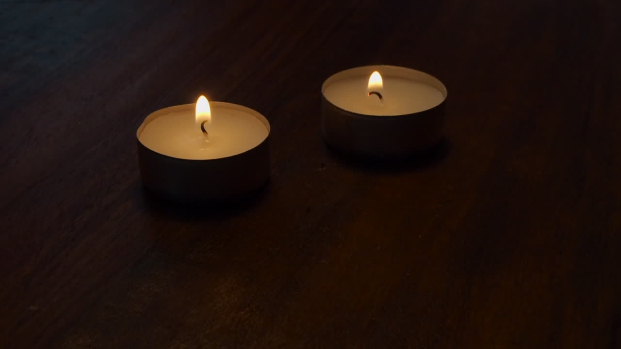 Room lights are dimmed as two tea light candles burn on wood table top