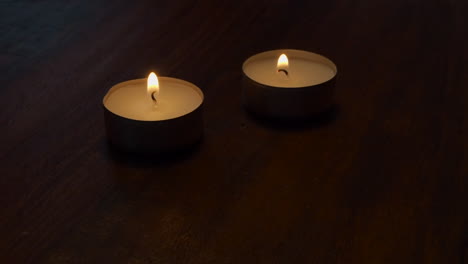 room lights are dimmed as two tea light candles burn on wood table top