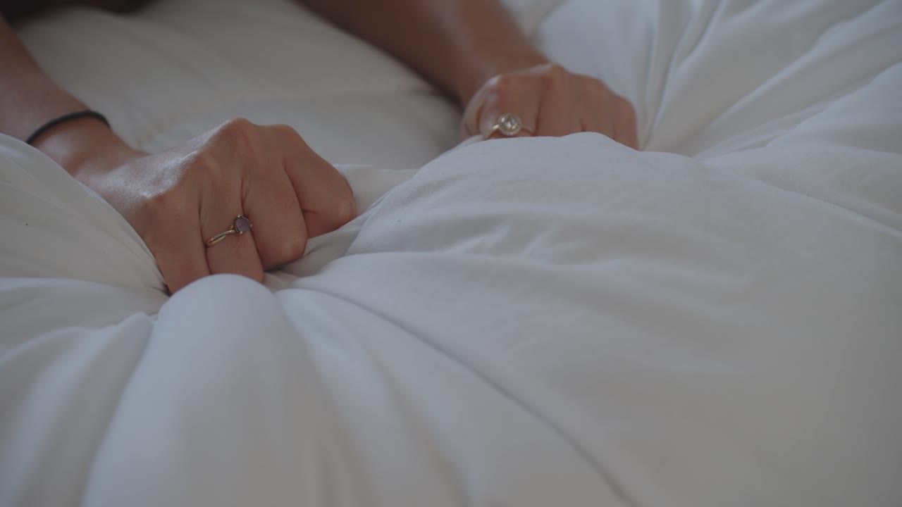 dama sensual manos comprimiendo sábanas de edredón blanco