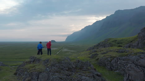 Birds-eye-orbit-of-three-people-tourist-on-top-of-peak-in-Iceland-highlands-taking-picture-amazing-panorama.-Drone-view-sportive-hikers-taking-photo-using-camera-on-top-of-cliff-nordic-countryside