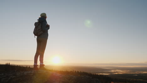 a woman traveler stands on top of a mountain looks at the beautiful landscape ahead admires the natu