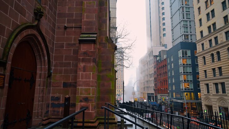 New York, USA, 25 dicembre 2025: Vista strada dalla Trinity Church nella bassa Manhattan. Si guarda giù per una strada cittadina dai gradini della chiesa con vapore e grattacieli.