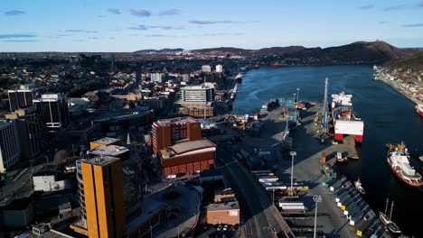 a drone flies over the downtown core of st. john's in newfoundland, showcasing tall office buildings, colourful hillside houses, and the harbour as evening light bathes the city