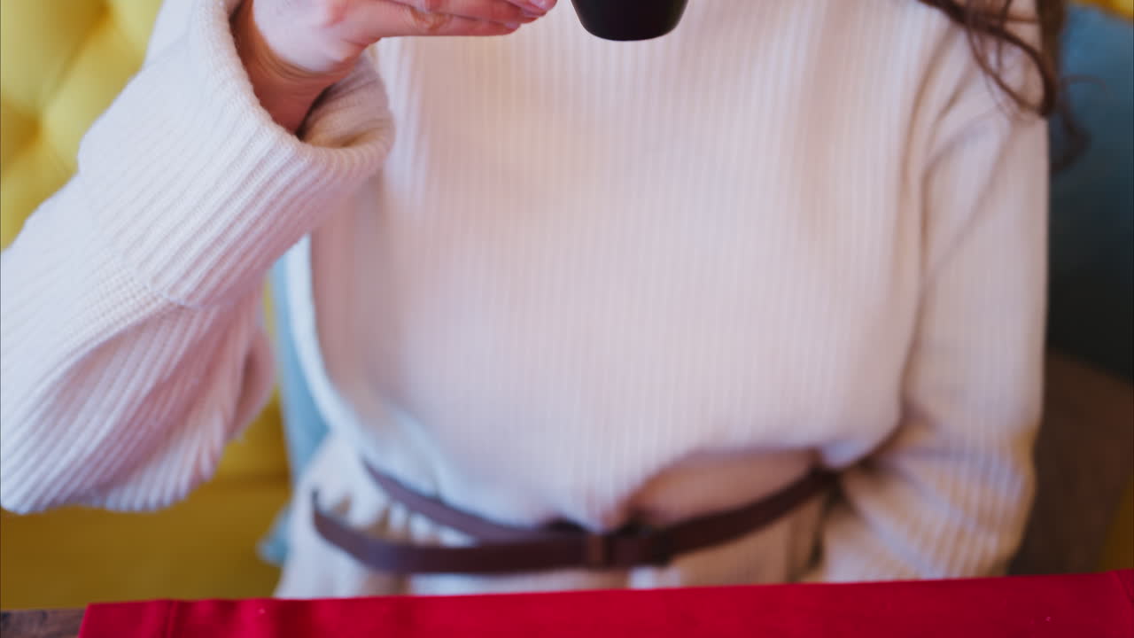 Close up of a woman holding an espresso in a black cup on a red tablecloth at a restaurant