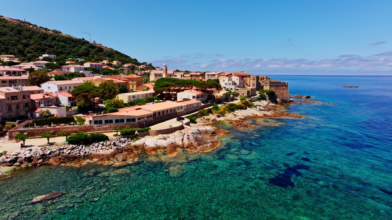 Aerial drone shot over the coastal town of Algajola in Balagne, Corsica, France. High view of the local town and the turquoise sea. Bright blue sky. Summer holidays destination