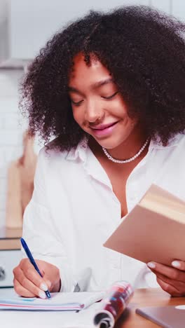 young happy african american woman writing notes in workbook and holding book