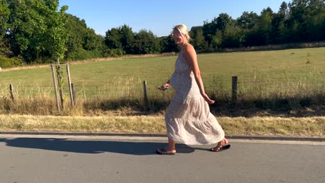 Toma-En-Cámara-Lenta-De-Mujer-Rubia-Embarazada-Caminando-Con-Flip-Flop-En-Camino-Rural-Durante-El-Día-Soleado---De-Cerca---Hermosa-Niña-Muy-Sonriente-Antes-Del-Nacimiento