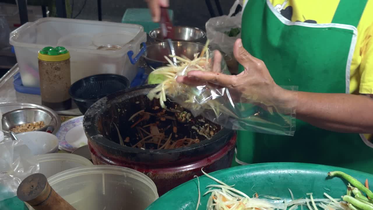 A street vendor skillfully prepares authentic som tam papaya salad, pounding fresh shredded papaya with chili, lime, fish sauce, and vegetables in a mortar for a flavorful Thai street food dish