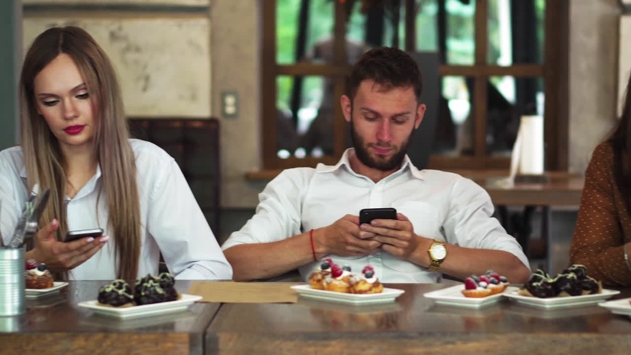 grupo multiétnico de amigos sentados en un restaurante y mirando cada uno del aburrimiento en su teléfono