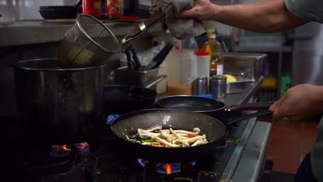 chef using a strainer straining noodles from a pot of boiling water, pour into frying pan, cooking veg aglio olio pasta, stir fried spaghetti with mixed mushrooms, garlic and olive oil in slow motion