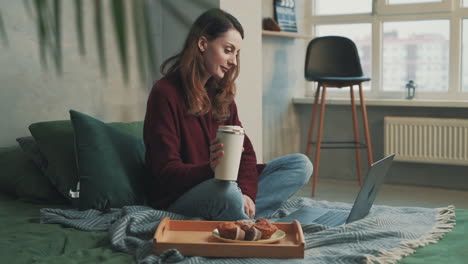 Una-Mujer-Bonita-Desayuna-Usando-Su-Laptop-Sentada-En-La-Cama-En-Casa