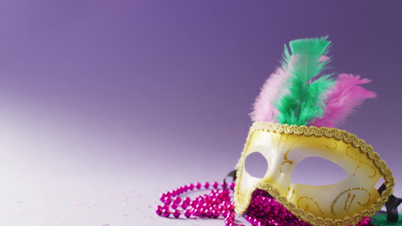 Video of carnival masquerade mask with feathers and pink mardi gras beads, with copy space