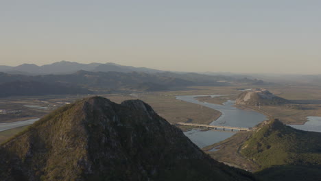 Landscape-view-of-a-river-estuary-with-several-pyramid-shaped-mountains-with-green-vegetation,-on-the-sunset