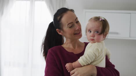 Caucasian-mother-playing-and-kissing-while-holding-her-baby-at-home