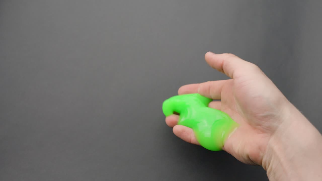 Close-up of green sticky slime being gently kneaded and held in a Caucasian hand.