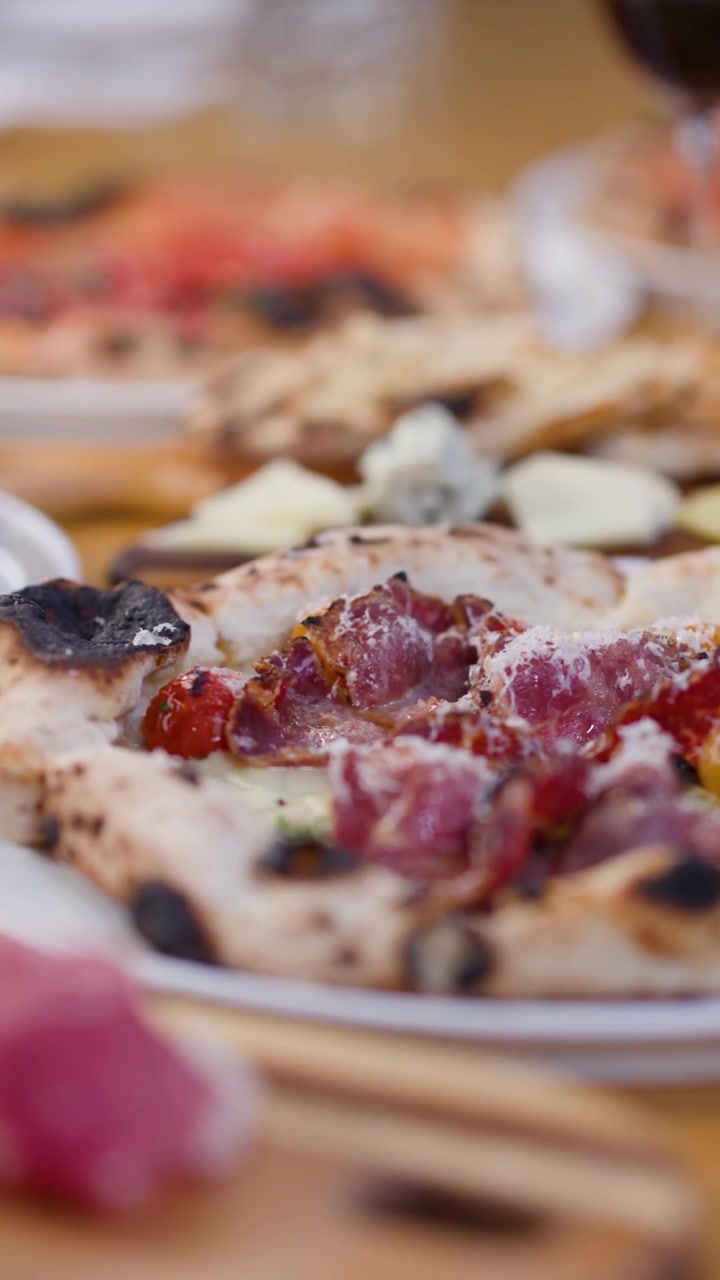 Panoramica ravvicinata di pizze a lievitazione naturale, prosciutto e vino rosso in un ambiente da ristorante